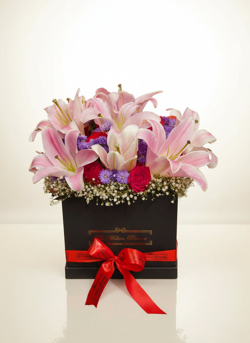 Elegant black box filled with pink lilies, vibrant red roses, and cheerful purple daisies, perfect for gifts or décor. Order stunning floral arrangements!